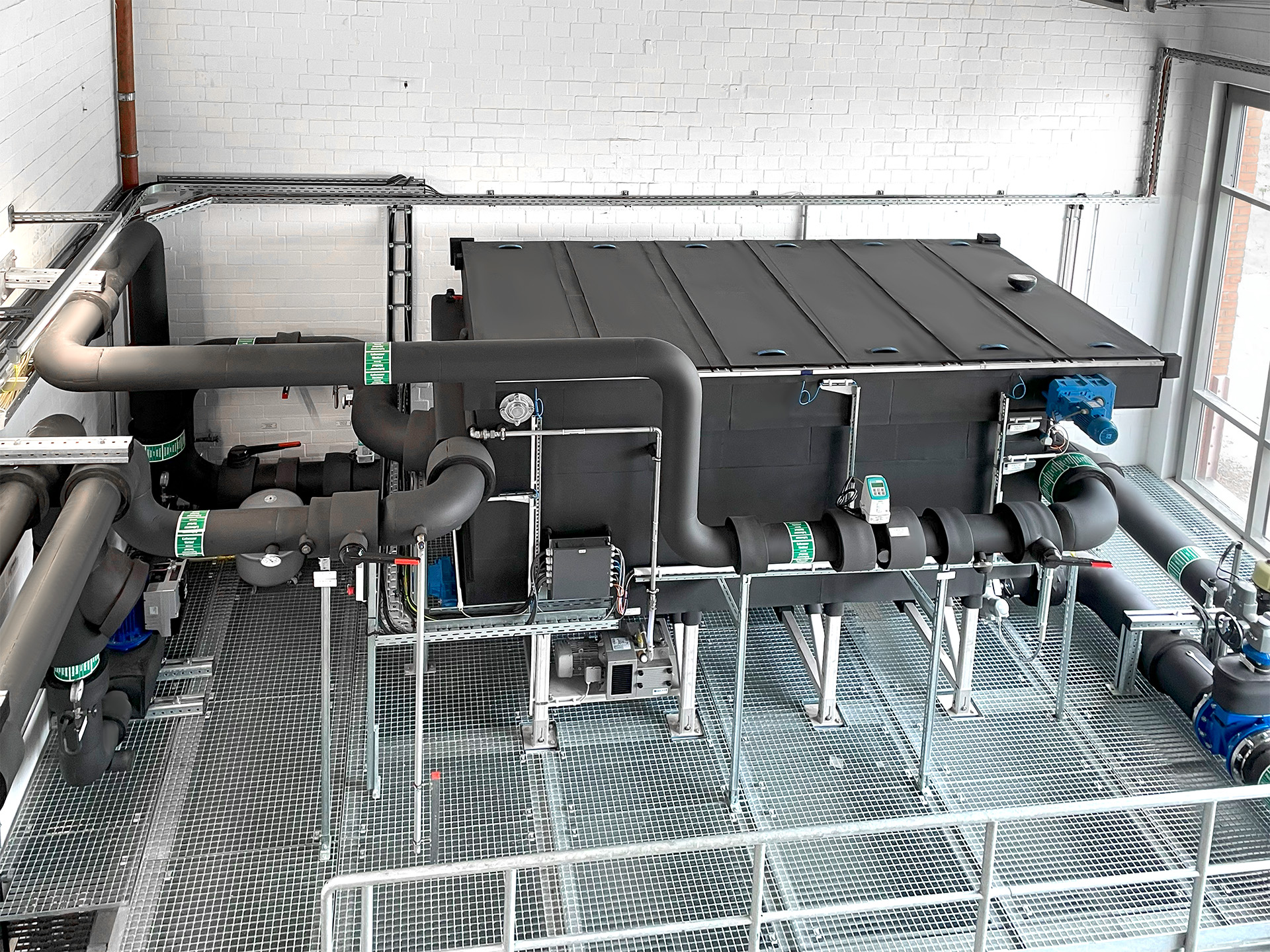 The HUBER RoWin14 wastewater heat exchanger, installed on a steel platform in the combined heat and power plant. Due to the condensation insulation, it does not have the typical stainless steel look but is black. (© SES Energiesysteme GmbH)