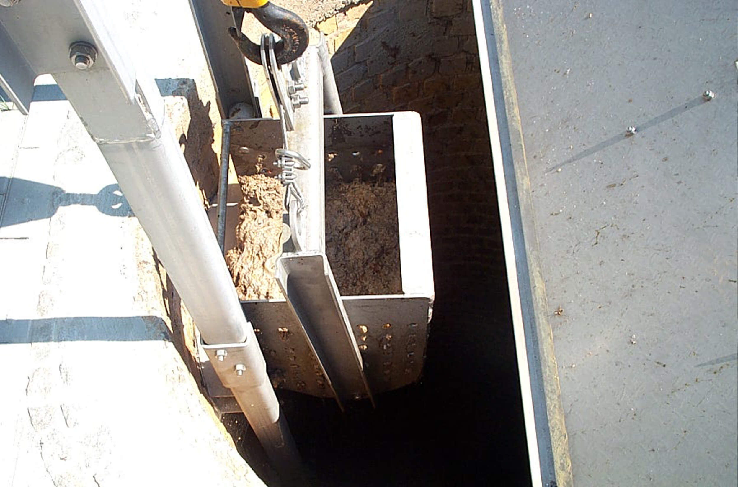 A screen basket filled with screenings, which is transported upwards to the discharge point by means of an electric chain hoist.